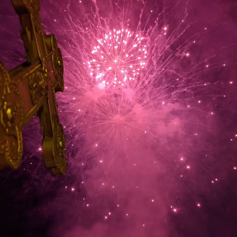 Fireworks bursting in the night sky beside a gilded Orthodox cross